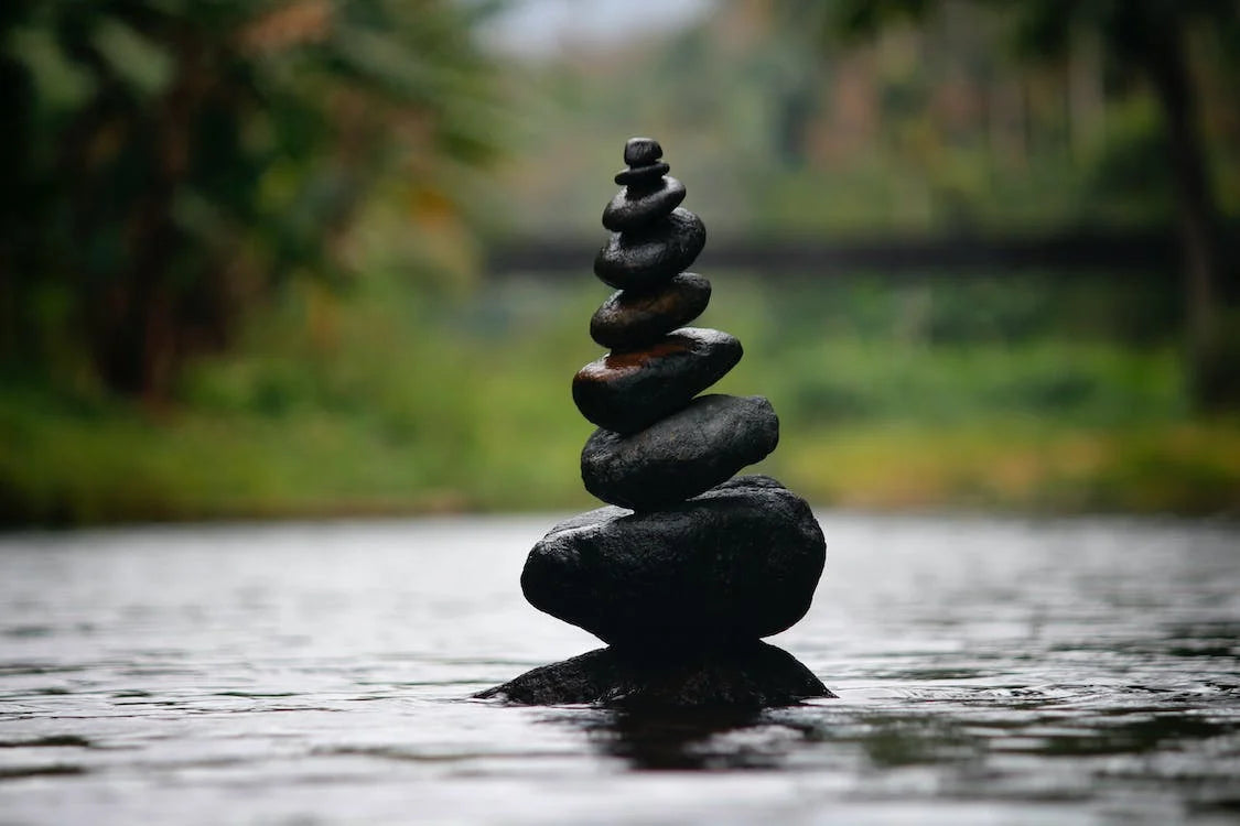 Stones places on top of each other, emerginf from a river next to a forest.